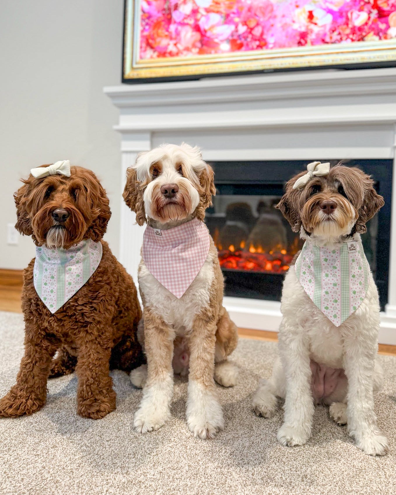 Three dogs wearing bandanas sitting in front of a fireplace.